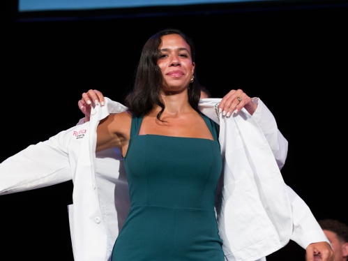 A new medical student pulls on a lab coat during the white coat ceremony