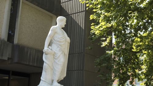 A statue of Hippocrates stands among green trees and buildings on campus