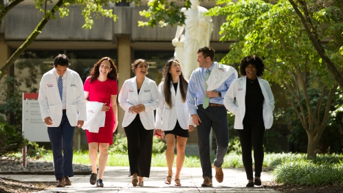 Medical school students don their new white coats while walking in front of the Hippocrates sculpture on campus