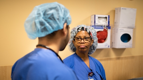 Doctors in blue scrubs and hairnets talk in a hospital hallway