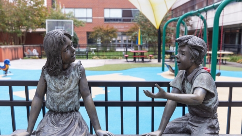 Bronze statues of two children outside a play area at the Child Health Institute