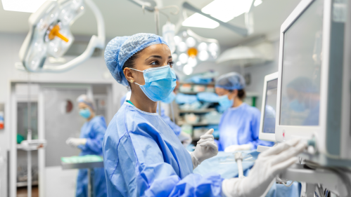 Anesthetist working in operating theatre wearing protecive gear and checking monitors while sedating patient before surgical procedure in hospital