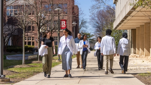 Medical school students walk on a sidewalk on Busch Campus