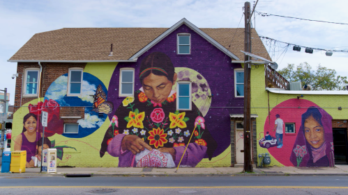 A mural on the side of a building in New Brunswick depicts a girl sewing