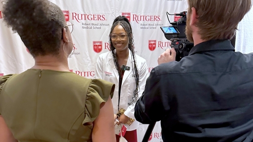 A student poses for a photo in front of the RWJMS logo backdrop at the White Coat ceremony