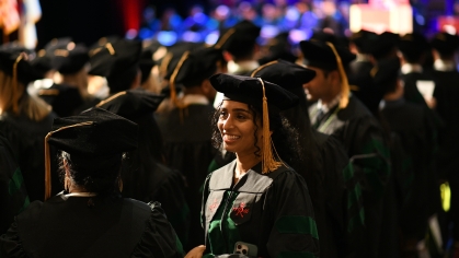  A graduate wearing a cap and gown smiles at commencement amid the crowd