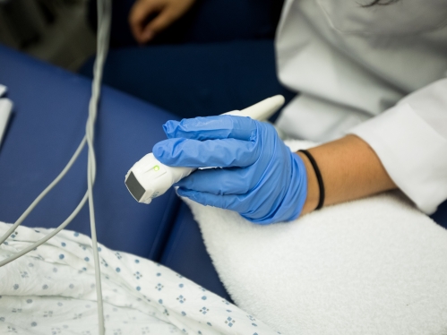 A close-up of a gloved hand holding a cardiac echo wand next to a patient