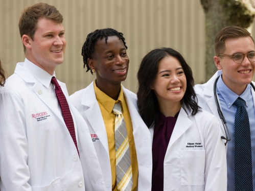 A group of medical students, in white coats, smiling for a picture.