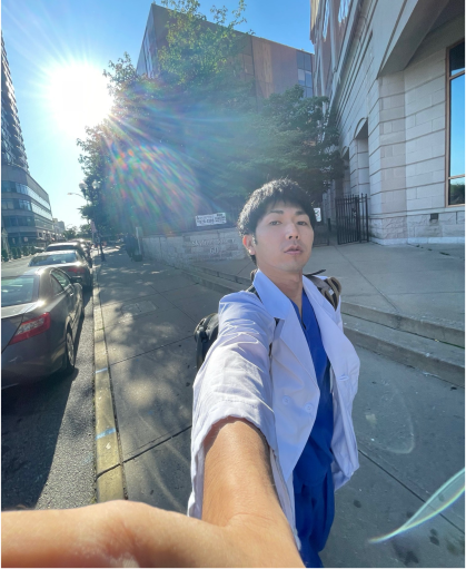 International student Kai Okubo takes a selfie on a sidewalk in New Brunswick with the sunshine behind him