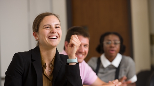 Three smiling students sit at a conference table