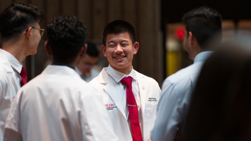 A group of medical students in white coats talk in the Great Hall