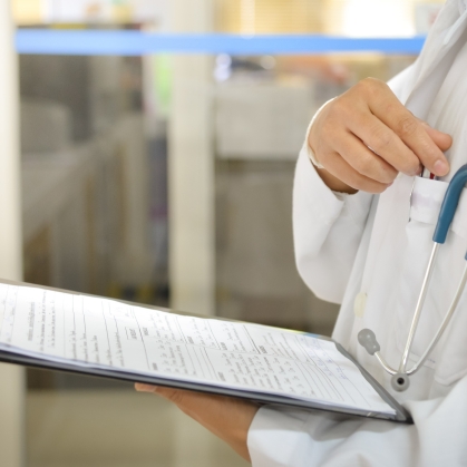 A doctor reaches for a pen to fill out forms on a clipboard