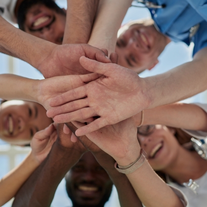 Health care workers stack their hands in a circle to signify teamwork and collaboration
