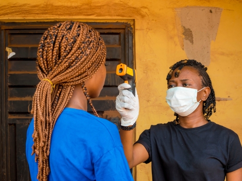 A health care worker wearing a mask and gloves takes a person's temperature